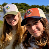 The Hay sisters wearing matching Mac's hats with a logo, standing outdoors near water.